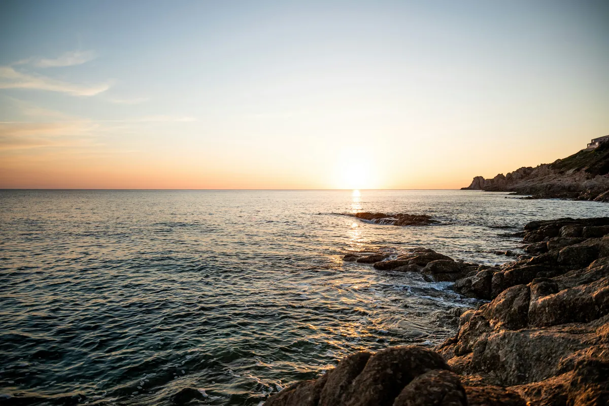 Sun setting over a calm sea beside a rocky shore