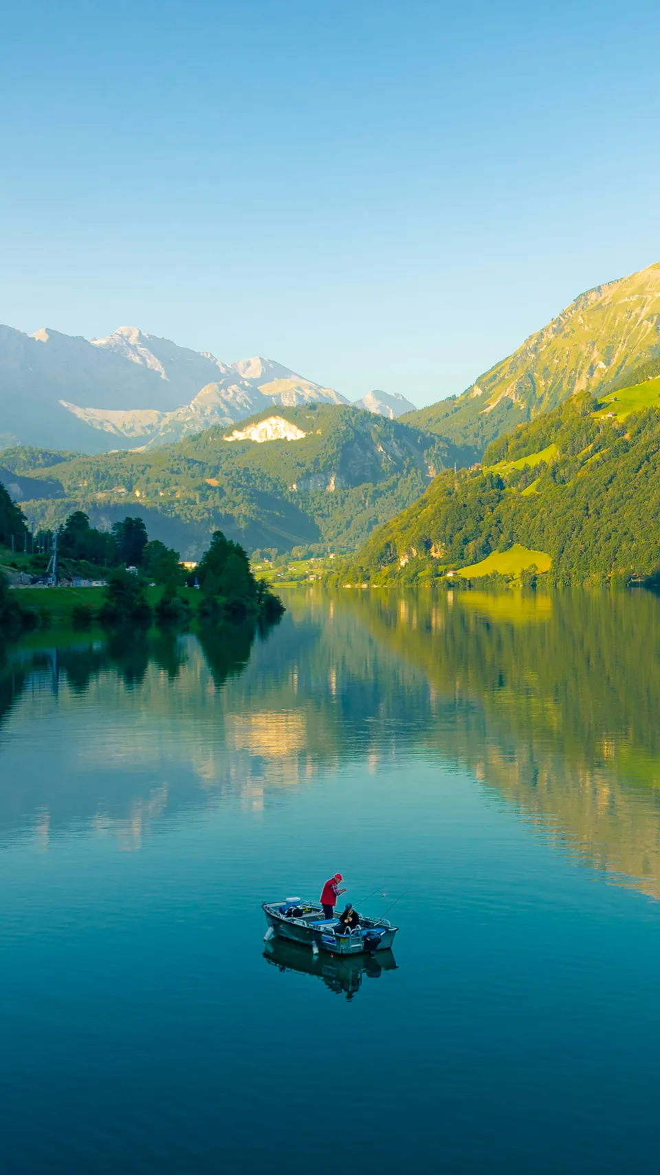 Small boat on a still alpine lake below green mountains